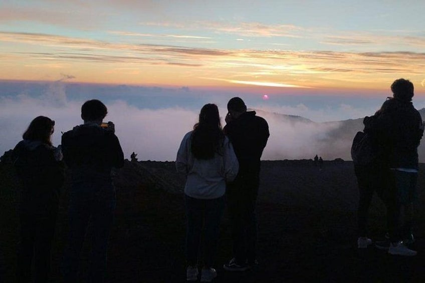 Un gruppo di persone in cima a una collina con vista su una valle, sullo sfondo un tramonto. 2