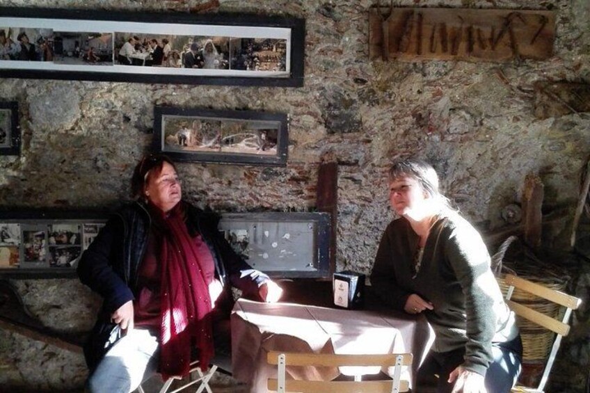 Two people sitting at a table in a rustic room with stone walls and framed pictures. 2