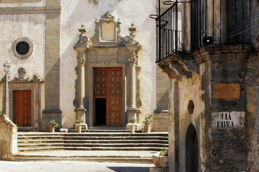 Un edificio storico con porte decorate, gradini che conducono all'ingresso e un cartello con la scritta 'VIA ROMA'. 3