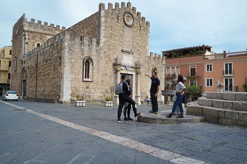 A historic stone building with a clock tower, a paved street, and pedestrians. 3