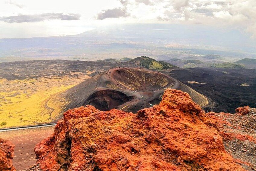Un cratère volcanique avec une route qui y mène, entouré d’un paysage rougeâtre et de collines lointaines. 3