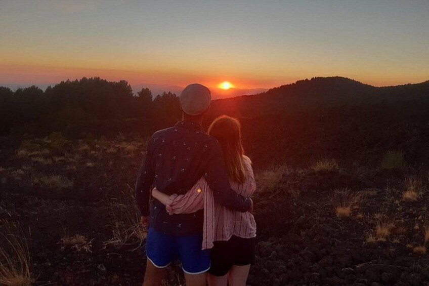 A couple standing on a hill overlooking a sunset. 2