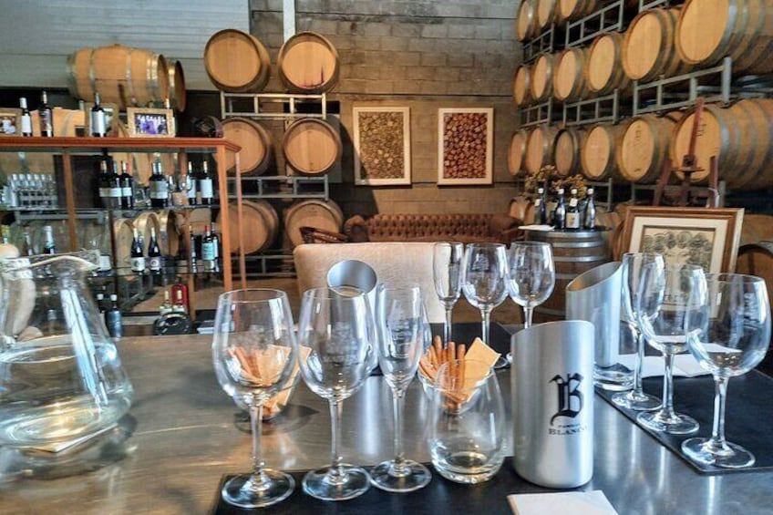 Una sala de degustación de vinos con copas vacías, un cubo plateado y barriles de madera al fondo. 1