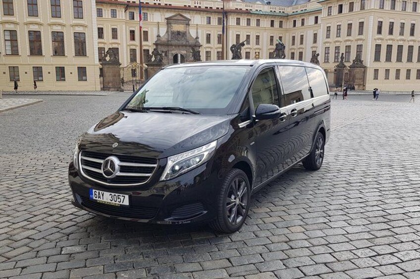 Un fourgon noir de marque Mercedes-Benz était garé sur une rue pavée, devant un bâtiment historique orné de statues et de colonnes. 2