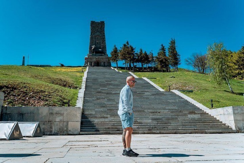 A man standing on a paved area with a large staircase leading to a tower-like structure. 5
