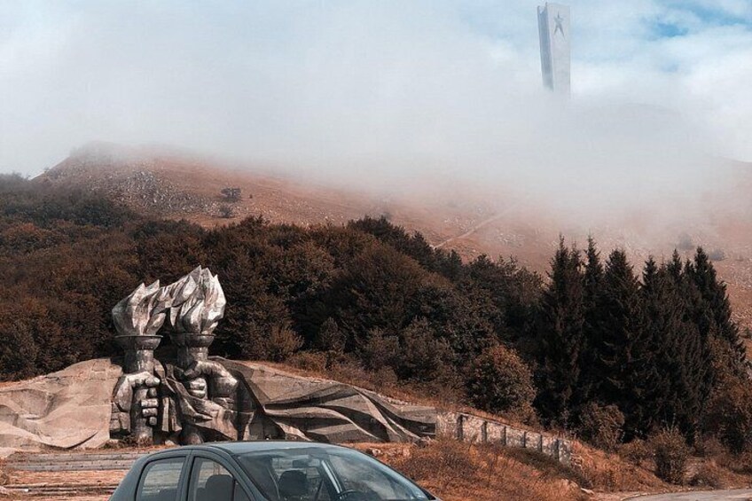 A mountainous landscape with a statue, a car, and a tower in the distance. 3