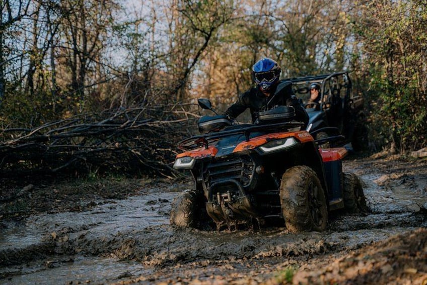 An off-road vehicle navigating a muddy trail in a wooded area. 2