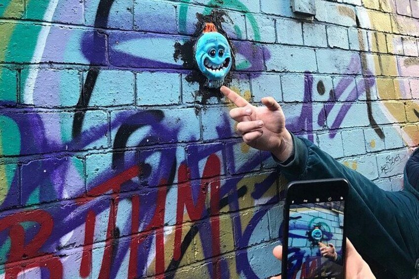 En hånd peger på en væg dækket af graffiti, hvor et tegneserieansigt og ordet 'BRINE' kan ses. 2