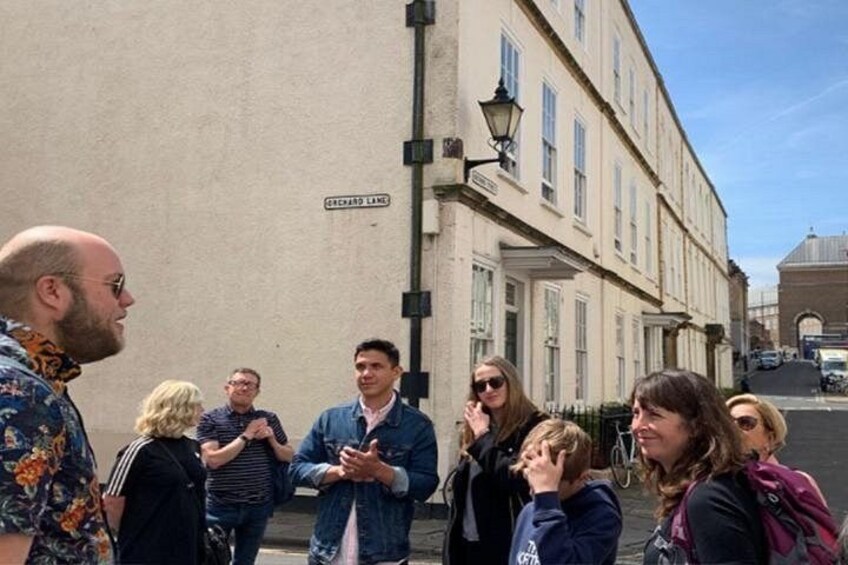 A group of people standing on a street in front of a building with a sign that reads 'GARDEN LANE.' 2