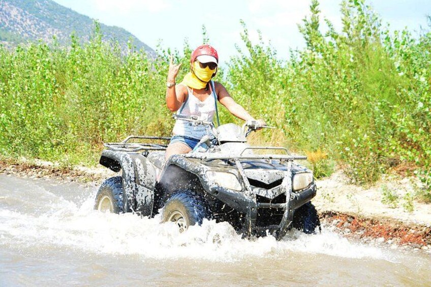 A person riding an ATV through a shallow water body with vegetation on the sides. 2