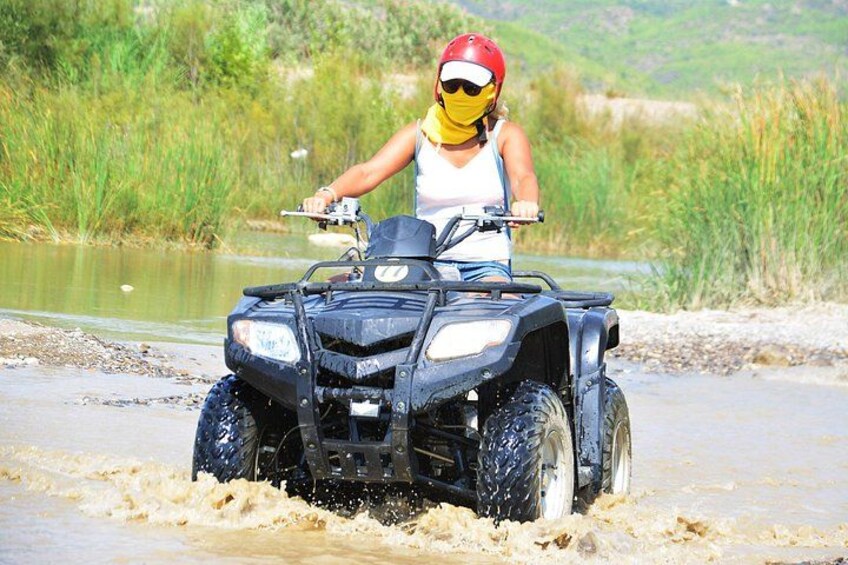 A person riding an ATV through a muddy water crossing. 4