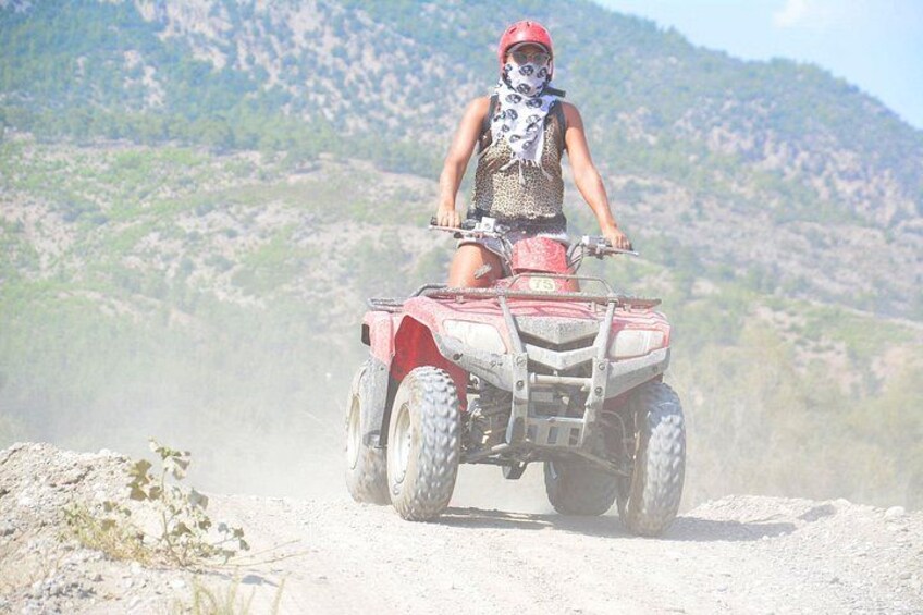 A person riding a red ATV on a dirt path with a mountainous landscape in the background. 1