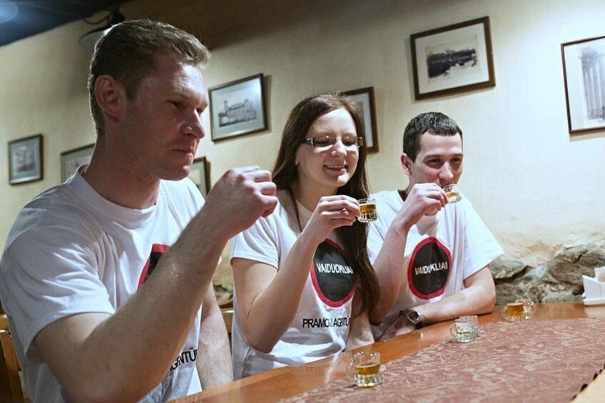 Tre persone sedute a un tavolo con bicchieri di birra, indossano magliette identiche con un logo. 1