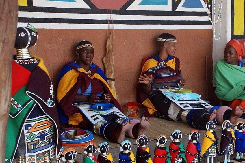People in traditional attire, a wooden structure, and various colorful items. 2