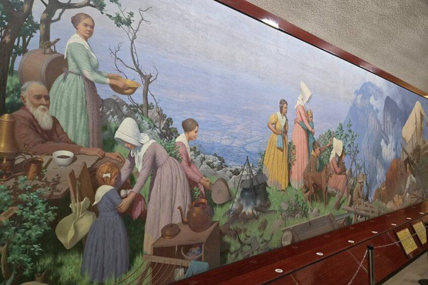 Un mural que representa una escena rural con gente realizando diversas actividades como cocinar, recoger y socializar. 3