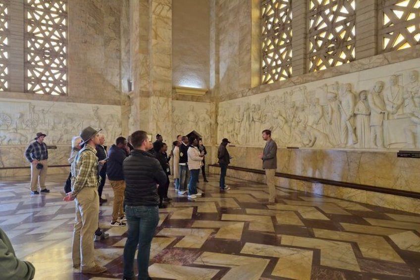Interior de mármol con un grupo de personas observando un relieve escultórico. 4