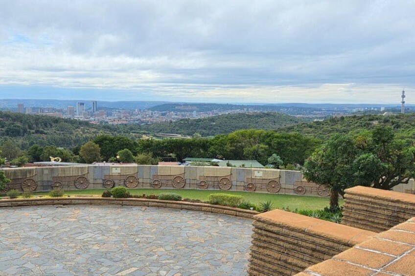 Un sendero de piedra, un jardín circular y un paisaje urbano distante con una torre destacada. 5