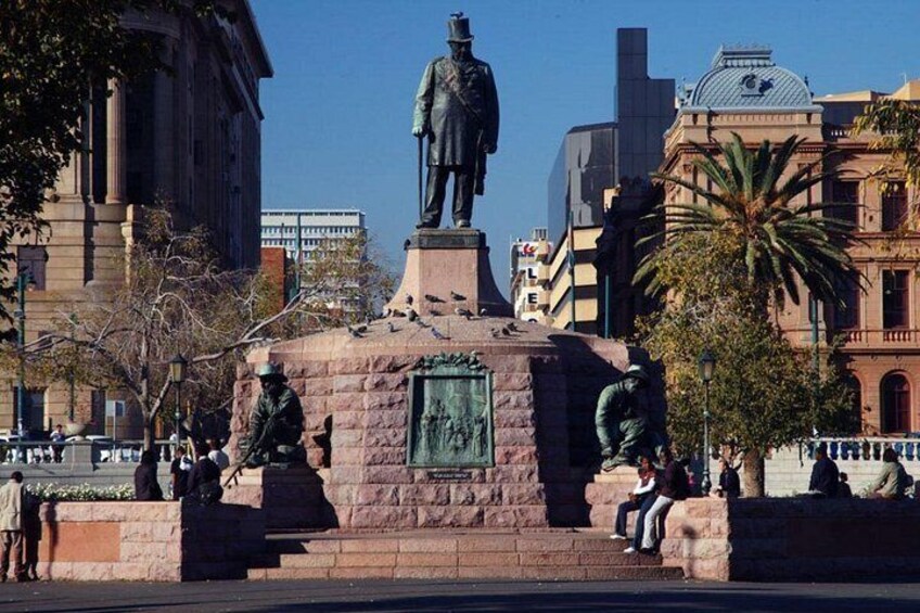 Una estatua de un hombre sobre un pedestal en una plaza urbana, con edificios al fondo. 3