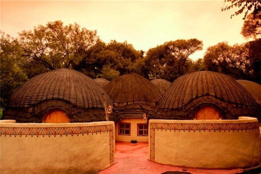Traditional thatched-roof huts with patterned walls, surrounded by trees. 2