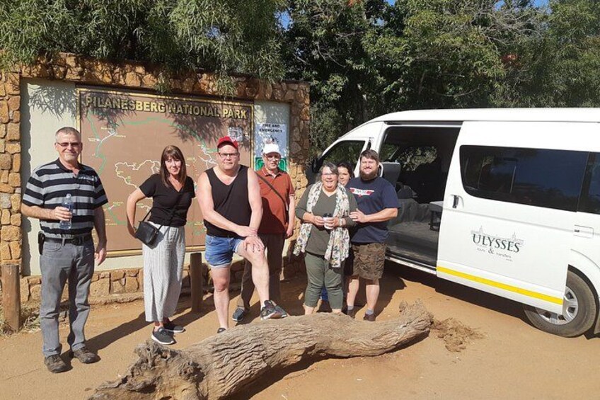 A group of people standing in front of a sign for Filanesberg National Park with a white van labeled 'ULYSSES' parked nearby. 2