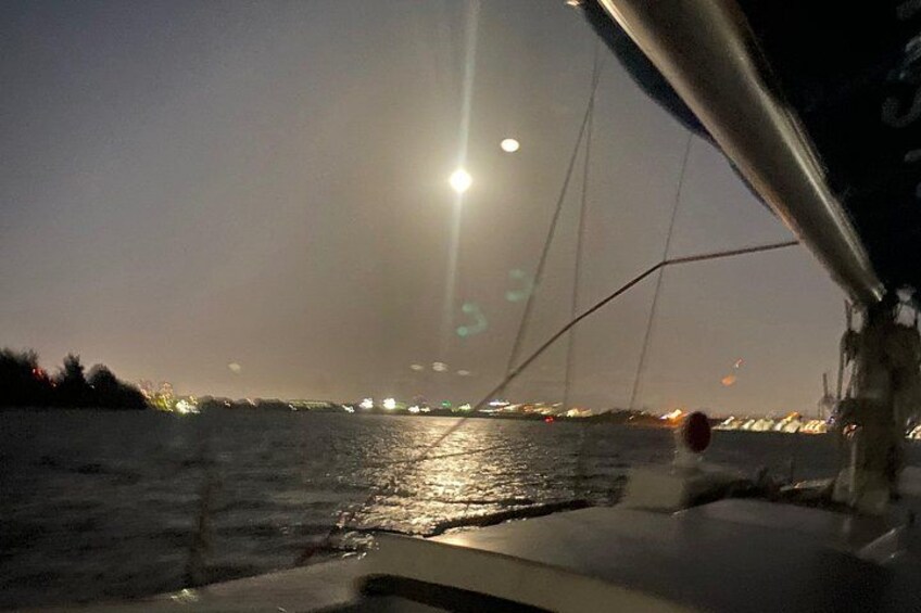 Une vue nocturne prise depuis un bateau, avec la silhouette d’une ville en arrière-plan et un pont au premier plan. 2