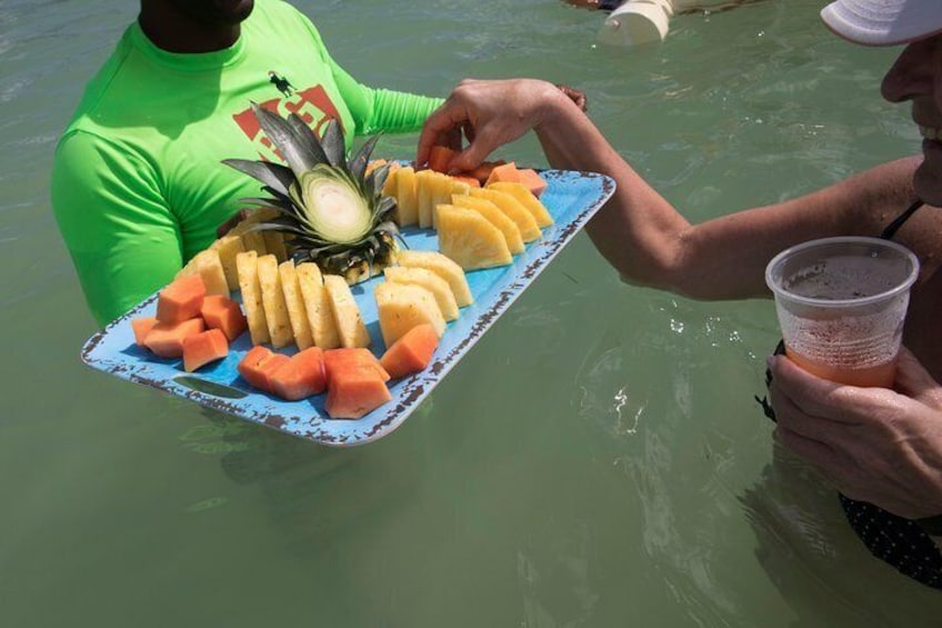 Eine Person hält eine Tablett mit Obst und einem Getränk in einem Gewässer. 4
