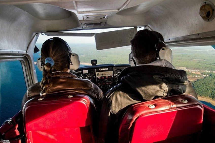 A cockpit with two pilots, a control panel, and a view of the landscape through the windshield. 1