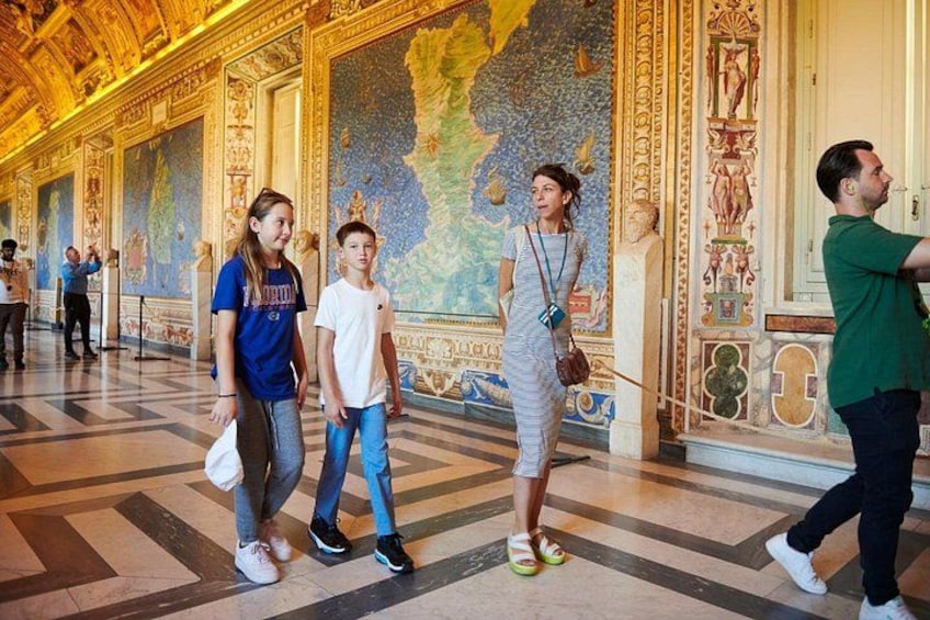 A group of people walking in a grand hall with ornate ceiling and detailed wall paintings. 1