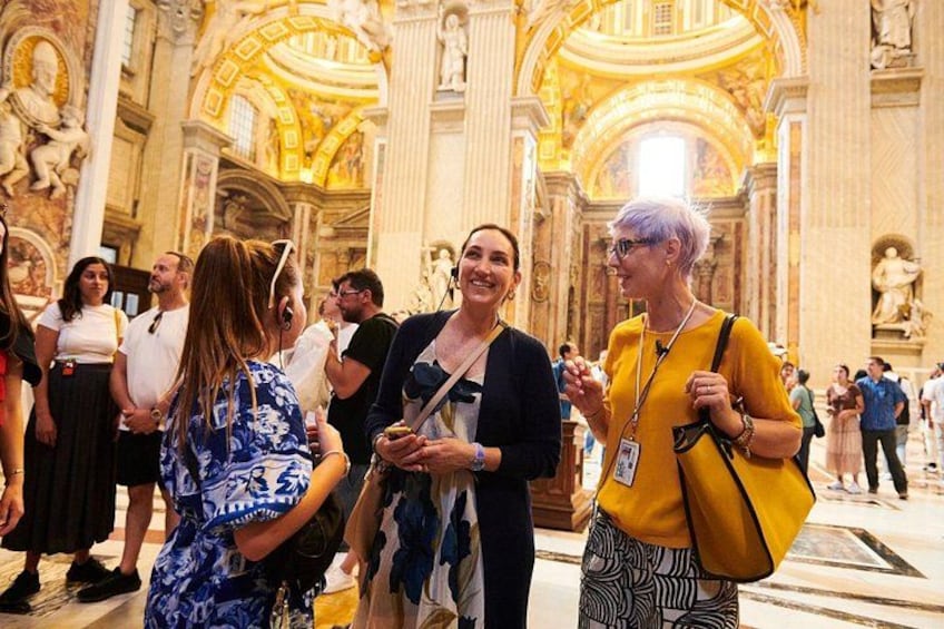 A group of people inside a grand building with ornate architecture, including columns and a high ceiling. 3