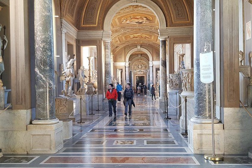 A grand hallway with marble columns, statues, and a long corridor. 5