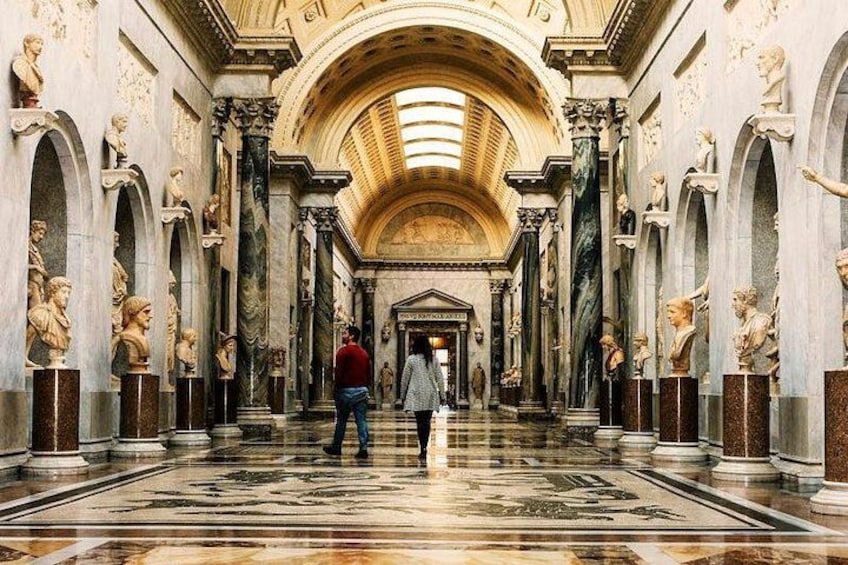 A grand hallway with marble columns, statues, and a high ceiling. 1