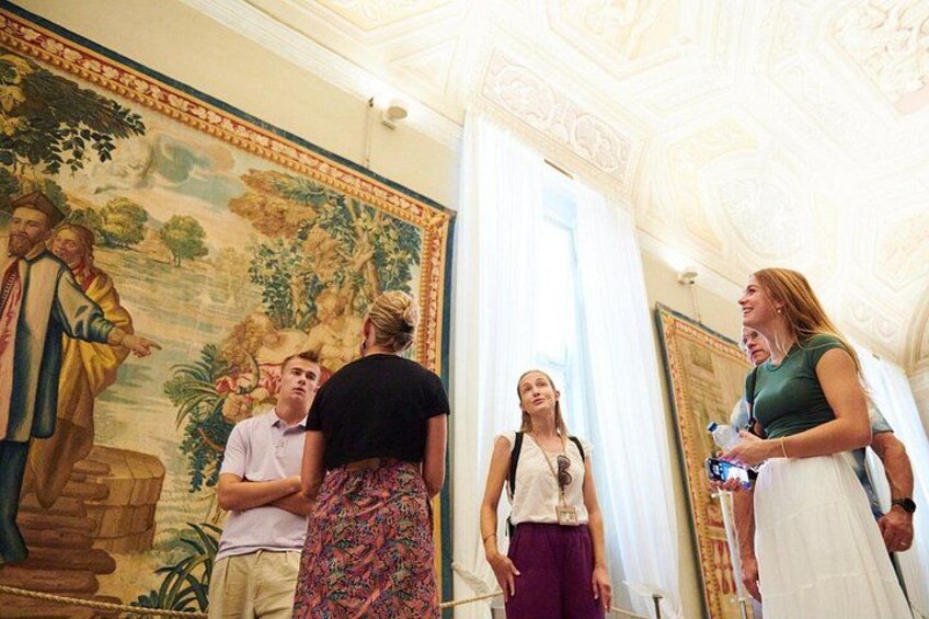 A group of people in a room with a large mural and ornate ceiling. 3