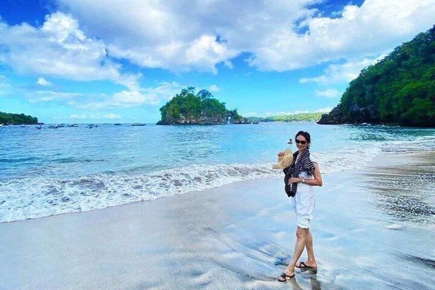 A beach with clear water, a person holding a drink, and a distant island. 4