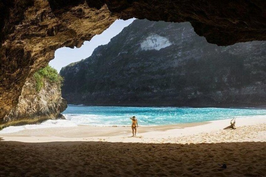 A beach with a cave entrance, a person standing, and another person sitting on the sand. 3