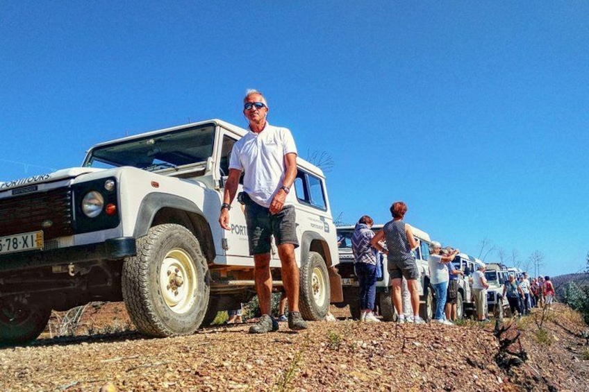Un grupo de vehículos todo terreno estacionados en un camino de tierra, con gente de pie a su lado. 1