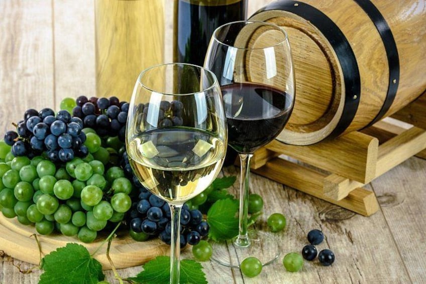 A wooden barrel, a glass of white wine, and a glass of red wine, with grapes and leaves in the foreground. 2