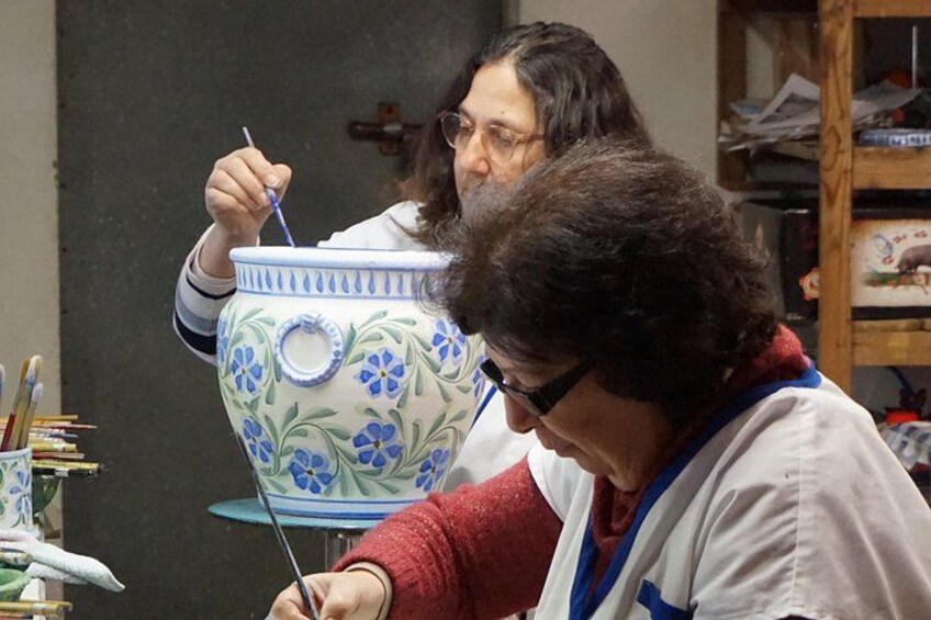Two people painting a large ceramic pot with floral designs. 4