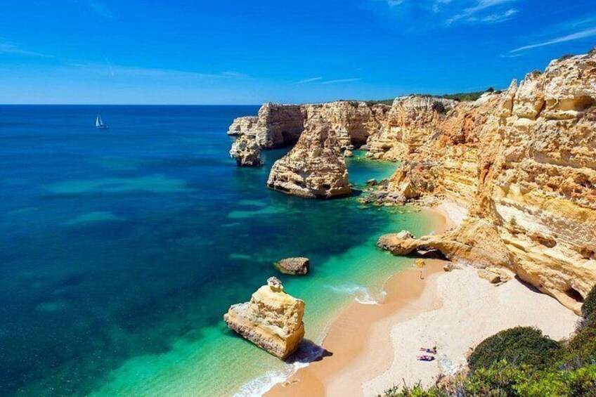 A coastal landscape with cliffs, clear turquoise waters, and a sandy beach. 3