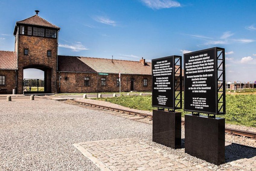 Een historisch gebouw met een bakstenen toren en een gebogen ingang. Er staan informatieborden ervoor. 5