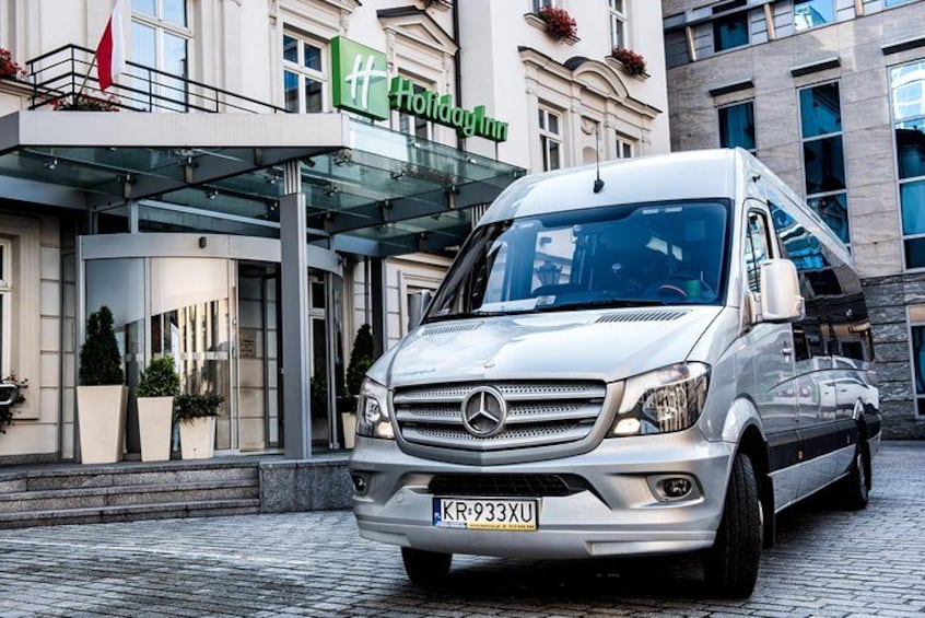 A white Mercedes-Benz van parked in front of a hotel with a glass entrance. 3
