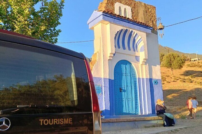 Un edificio bianco con una porta blu e una piccola torre, un'auto parcheggiata e una persona sullo sfondo. 3