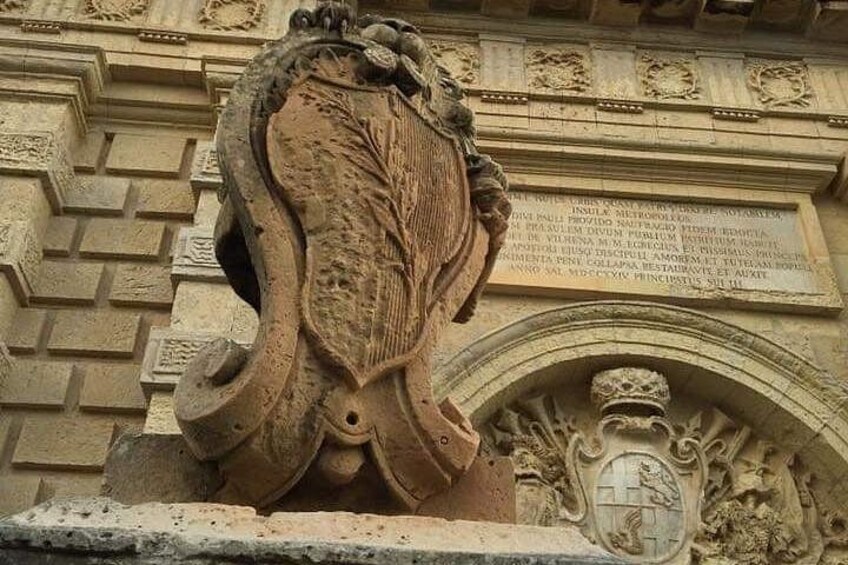 A stone sculpture with a shield and crest, part of a building's facade. 3