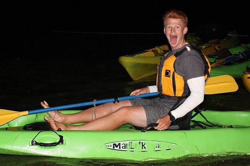 A person sitting on a green kayak with a life jacket, holding a paddle, and wearing a helmet. 1