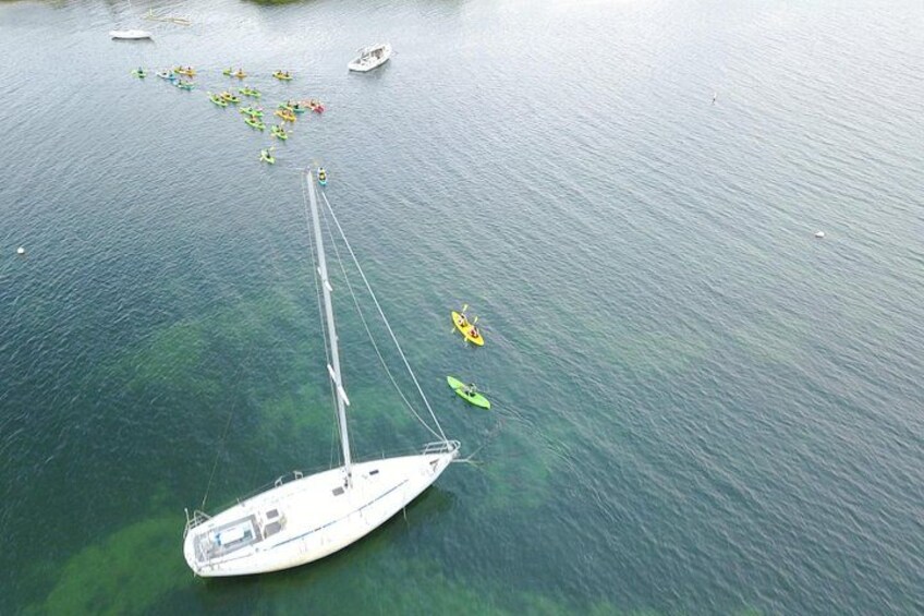 A sailboat anchored in calm waters with several kayaks nearby. 5