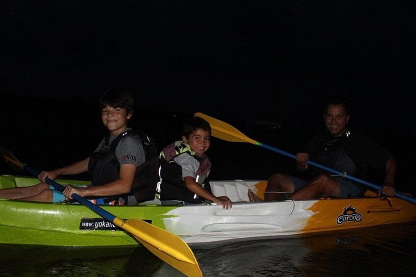 Three people in a kayak on a body of water at night. 3