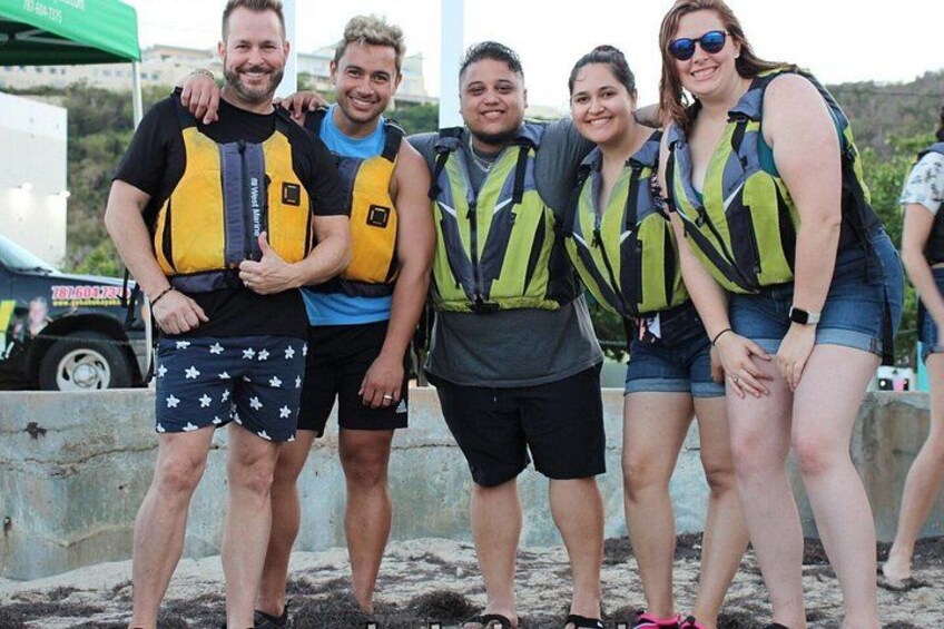 A group of people wearing life jackets standing on a sandy beach. 4