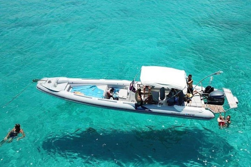 A white inflatable boat with people on it, floating on clear turquoise water. 5
