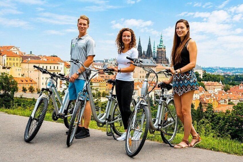 Three people standing next to bicycles with a cityscape in the background. 3