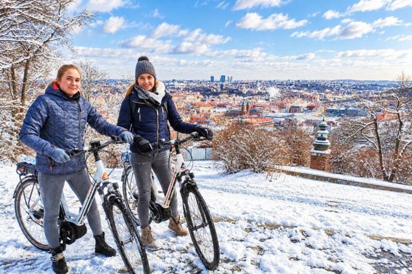 Two people on bicycles on a snowy hill with a cityscape in the background. 5