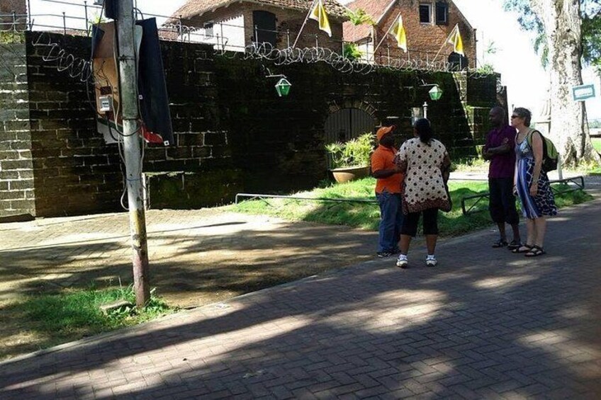 A paved pathway, a brick wall, and a group of people standing and conversing. 1